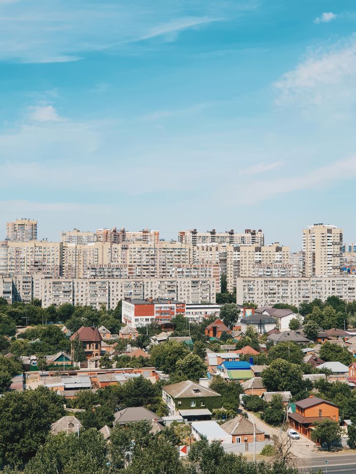 A vibrant cityscape featuring tall residential buildings and lush greenery under a bright blue sky.